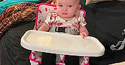 Sofia joined the competition — help win amazing prizes! baby, black_fabric, blanket, chair, child, clothing, couch, cushion, furniture, high_chair, home, indoor, living_room, person, pink, seat, serious_face, striped_pillow, table, young_child