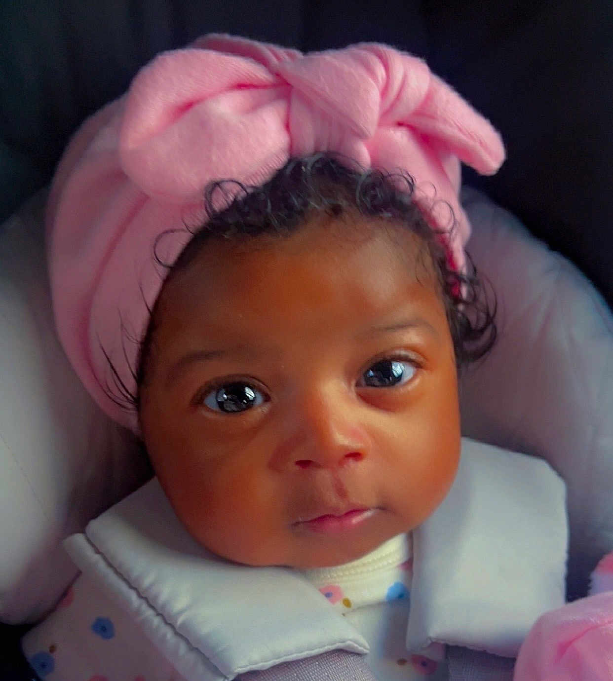 Amily joined the competition — help win amazing prizes! baby, infant, portrait, headband, pink, closeup, face, child, cute, curly_hair, clothing, indoors, seatbelt, car_seat, expression, soft_light, skin, young_child, person, eyes