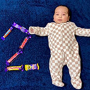 Manveer is registered to the contest to win money with this photo: baby, blue_blanket, candy_bars, checkered_pattern, child, comfortable, cute, face, indoor, infant, lying_down, number_two, onesie, portrait, relaxed, sleepwear, smiling, soft_texture, sweet_treats, young_child