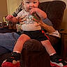 toddler, child, baby, sitting, shoes, socks, toy_story_shirt, hands, armchair, furniture, indoor, person, face, legs, clothing, home, curious, supporting_hands, casual, cozy