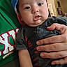 baby, child, infant, cap, blue_cap, hand, person, adult_hand, clothing, green_shirt, indoor, living_room, furniture, curious, cute, portrait, people, holding, casual, home