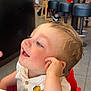 toddler, child, smiling, blonde_hair, high_chair, white_shirt, cartoon_character, indoor, restaurant, table, people, seated, casual, happy, portrait, side_view, red_chair, playful, food_stains, family
