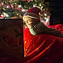 Gideon is registered to the contest to win money with this photo: baby, santa_hat, christmas_tree, book, blanket, holiday, red, festive, child, smiling, decorations, cozy, indoors, warm_lighting, christmas, reading, face, cute, seasonal, happy