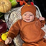 baby, infant, orange_clothing, turkey_hat, blanket, autumn, pumpkin, vegetables, onion, sweet_potato, carrot, tray, smiling, face, indoors, cozy, festive, holiday, cute, child