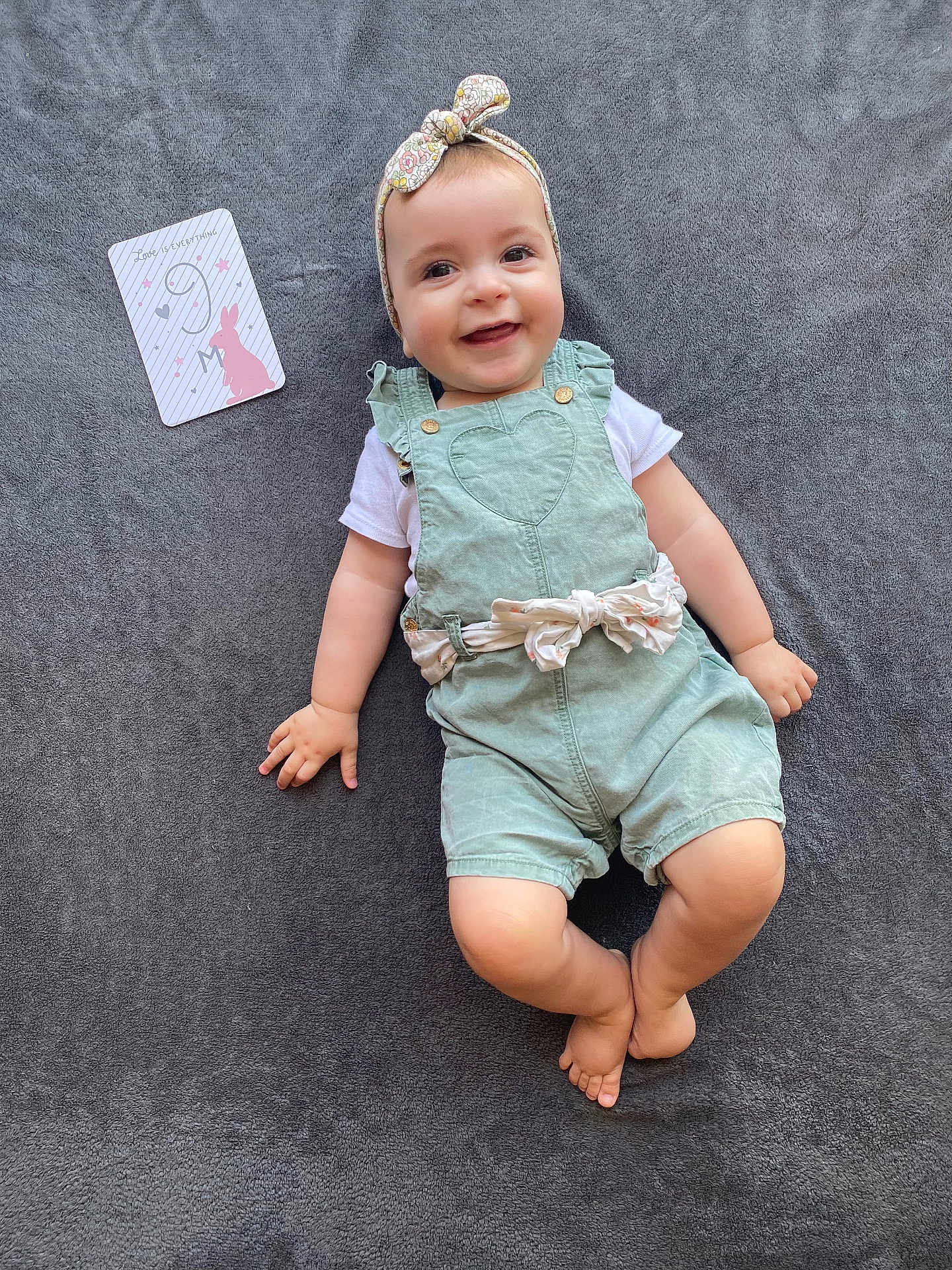 Léna participe au concours pour gagner de l'argent avec cette photo : baby, smiling, headband, romper, green_clothing, blanket, card, bunny, pastel_colors, cute, happy, infant, child, portrait, soft_texture, lying_down, indoors, playful, adorable, toddler