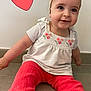 Léna a rejoint le concours — aidez-le/la à gagner de superbes lots ! baby, child, infant, sitting, headband, floral, smiling, cute, red_pants, white_top, indoor, floor, heart_graphic, portrait, happy, young_child, casual_clothing, barefoot, girl, candid