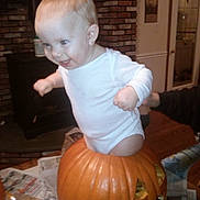 Mackenzie participe au concours pour gagner de l'argent avec cette photo : baby, child, pumpkin, halloween, carved_pumpkin, indoor, onesie, smiling, happy, face, person, hands, floor, newspaper, brick_wall, furniture, door, decor, head, playful