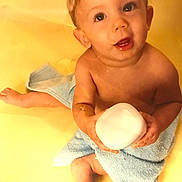 Joshua joined the competition — help win amazing prizes! baby, child, towel, bottle, skin, cute, sitting, looking_up, happy, innocent, blue_towel, yellow_background, barefoot, portrait, young_child, smiling, indoors, person, toddler, holding_object