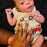 adult_hand, baby, black_background, clothing, curious, cute, expression, fingers, hand, infant, lying_down, newborn, person, protective, romper, skin, small_hands, soft_lighting, toddler, wide_eyes
