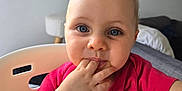 Amara a rejoint le concours — aidez-le/la à gagner de superbes lots ! baby, blue_eyes, casual, child, clothing, cute, expression, face, finger_in_mouth, furniture, high_chair, indoor, infant, looking_at_camera, person, pink_shirt, portrait, seated, short_hair, skin