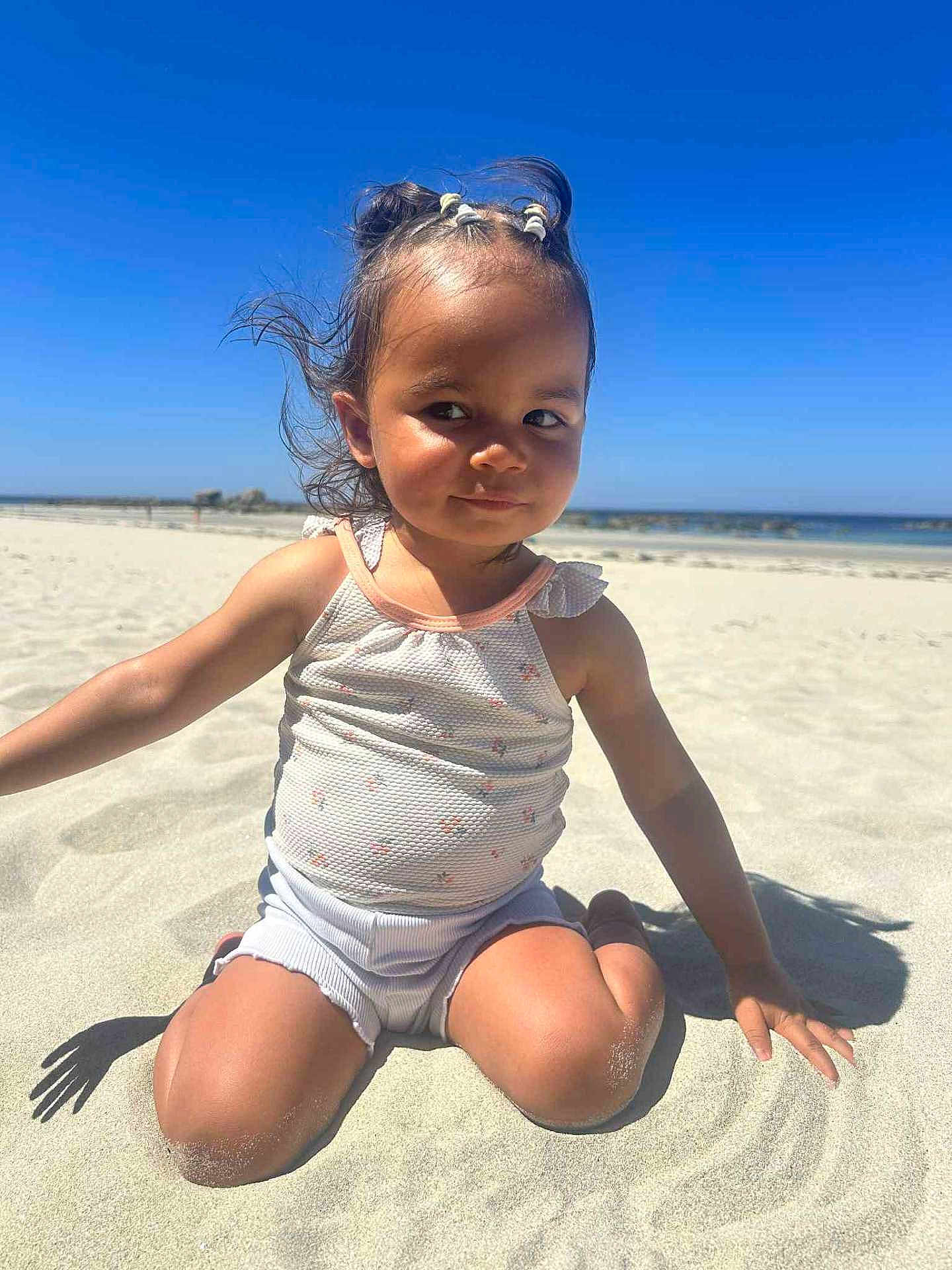 Théa participe au concours pour gagner de l'argent avec cette photo : child, toddler, beach, sand, sunny, outdoor, smiling, hair, braids, ocean, sky, summer, clothing, sitting, shadow, cute, portrait, playful, sunlight, happy
