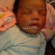 Ji'Ana is registered to the contest to win money with this photo: newborn, baby, sleeping, portrait, face, infant, blanket, swaddled, onesie, indoors, bed, cushion, resting, peaceful, closed_eyes, dark_hair, family, granddaughter, text_overlay, photograph