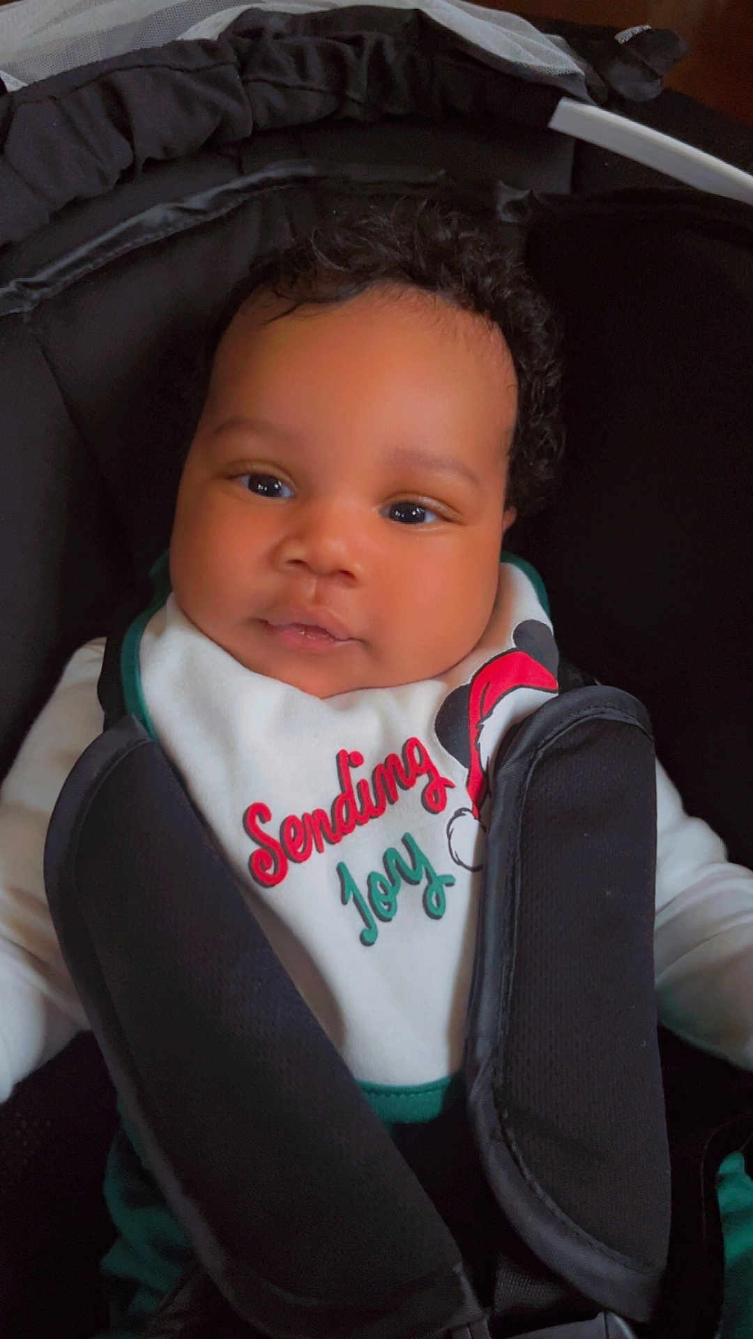 Jacques is registered to the contest to win money with this photo: baby, child, car_seat, curly_hair, bib, clothing, cute, face, infant, indoors, joy, person, portrait, sitting, smile, young_child, holiday_theme, black_hair, seat_belt, closeup