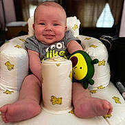Cohenn is registered to the contest to win money with this photo: baby, infant, smile, face, toy, avocado_toy, cushion, chair, teddy_bear_pattern, clothing, cute, indoor, happy, child, sitting, foot, skin, person, portrait, home