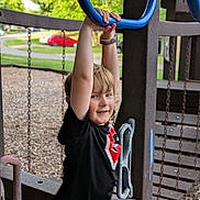 Tearston is registered to the contest to win money with this photo: child, boy, playground, playground_equipment, blue_rings, swing, smiling, outdoor, trees, grass, wood_chips, black_shirt, shorts, wristband, fun, active, daylight, park, happy, leisure