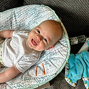 Jaxxon is registered to the contest to win money with this photo: baby, blanket, blue_blanket, carpet, child, closeup, comfort, cozy, cushion, cute, face, happy, indoors, infant, light_skin, patterned_fabric, seated, smiling, water_bottle, white_shirt