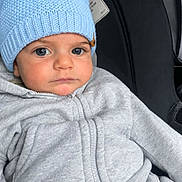 Adam Mostafa is registered to the contest to win money with this photo: baby, child, infant, car_seat, car, blue_hat, knit_hat, gray_clothing, jacket, zipper, portrait, face, eyes, serious_expression, sitting, indoors, close_up, travel, cozy, photography