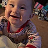 baby, child, smiling, happy, portrait, indoors, blanket, pajamas, clothing, face, eyes, hands, infant, sitting, toy_room, home, warm_lighting, close_up, joyful, photography