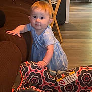 Nova joined the competition — help win amazing prizes! baby, child, toddler, standing, blue_dress, curious, face, portrait, indoors, living_room, couch, car_seat, furniture, folding_table, wood_floor, home, baby_gear, colorful_pattern, smiling, photography