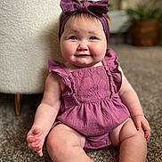 Rosie is registered to the contest to win money with this photo: adorable, baby, candid, carpet, child, chubby_cheeks, closeup, cute, furniture, happy, headband, home, indoor, infant, person, portrait, purple_outfit, sitting, smiling, soft_lighting