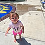 toddler, child, barefoot, pink_shorts, white_tshirt, cow_graphic, shadow, playground, concrete, sunny, outdoor, curious_expression, short_hair, rosy_cheeks, summer_clothing, play_area, bench, fence, slide, daylight