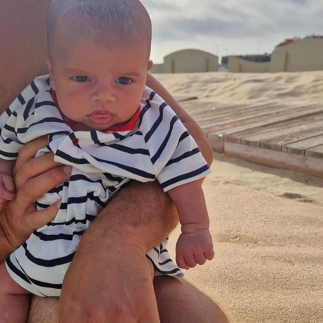 Lorenzo a rejoint le concours — aidez-le/la à gagner de superbes lots ! adult_hand, baby, beach, casual, child, clouds, cute, holding, infant, nature, outdoor, person, portrait, relaxation, sand, sky, striped_clothing, summer, sunlight, vacation
