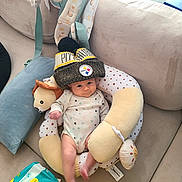 Noelle is registered to the contest to win money with this photo: baby, infant, beanie, hat, boppy_pillow, plush_toy, onesie, couch, cushion, backpack, baby_wipes, legs, arm, smile, face, living_room, soft_toy, seat, sun_pattern, cozy