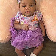 Maverick is registered to the contest to win money with this photo: baby, baby_girl, child, clothing, colorful, cushion, cute, flower_pattern, happy, headband, indoors, infant, onesie, portrait, purple, seated, small, socks, soft_texture, tutu