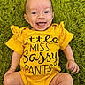 baby, child, smiling, yellow_onesie, text_on_clothing, green_rug, happy, infant, cute, portrait, laying_down, playful, human, face, skin, expression, sitting, candid, indoors, one_person