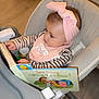 baby, book, child, curious, cute, face, floor, furniture, headband, high_chair, indoor, infant, learning, person, pink, reading, seated, striped_clothing, toy, young_child