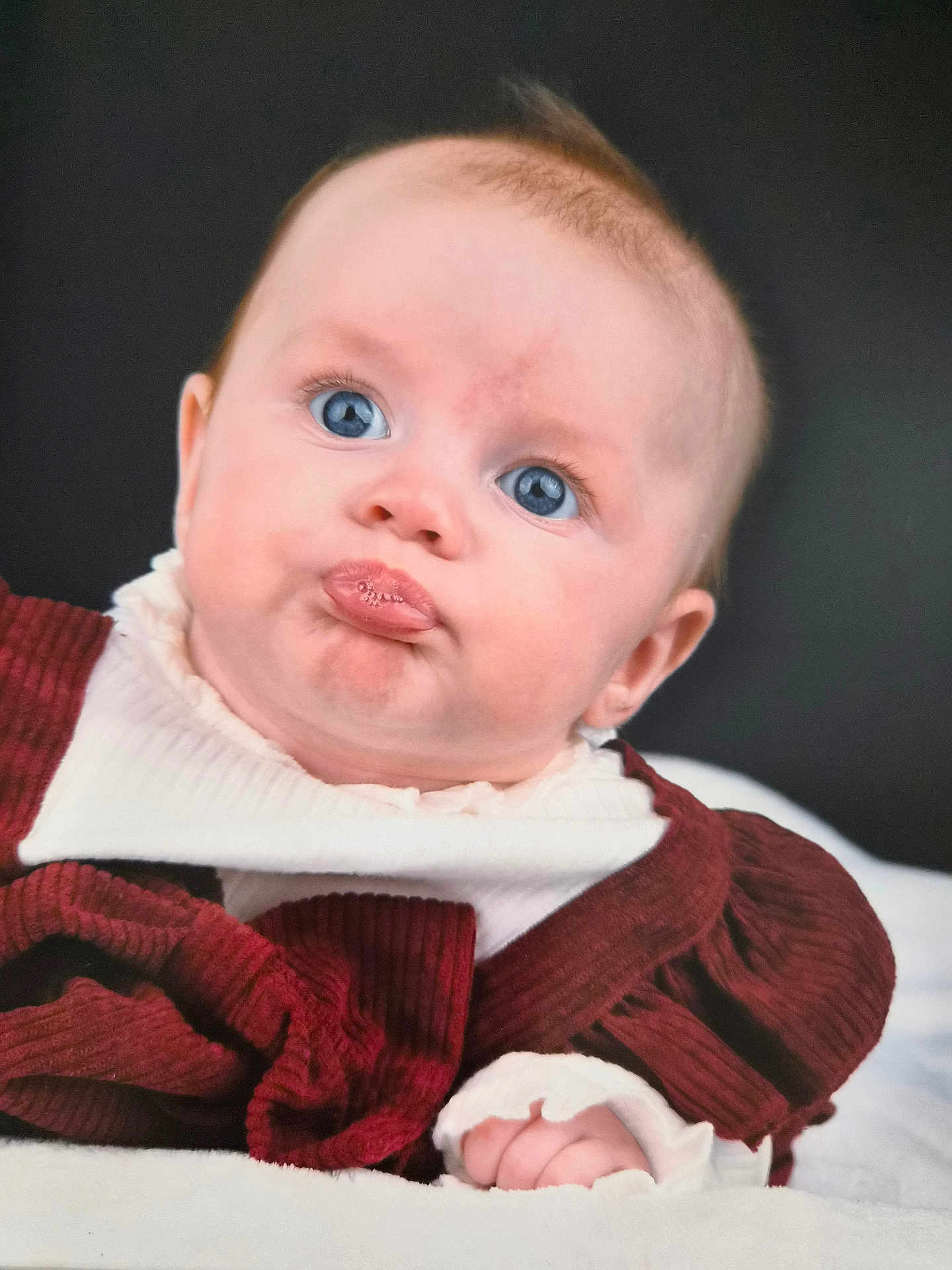 Lily joined the competition — help win amazing prizes! baby, infant, face, blue_eyes, pout, expression, clothing, maroon, white, cute, portrait, child, newborn, soft_lighting, indoors, person, skin, head, hand, background