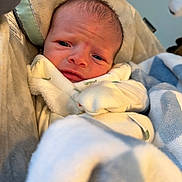 Jaxson is registered to the contest to win money with this photo: baby, bed, blanket, child, close_up, cozy, cute, eyes, fabric, face, indoors, infant, newborn, plush, portrait, sitting, sleeping_area, smiling, swaddled, warm_lighting