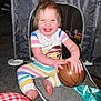 baby, child, smiling, basketball, striped_pajamas, wild_hair, play_area, toy, mesh_mat, floor, happy, indoor, cute, person, infant, fun, sitting, playful, colorful, grin