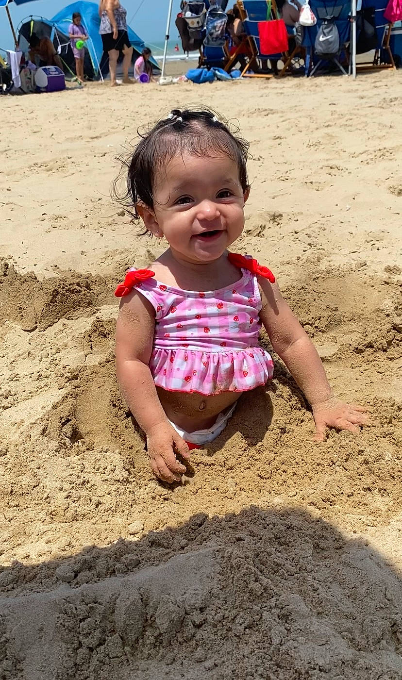 Selena is registered to the contest to win money with this photo: baby_toddler_clothing, beach, body_of_water, child, clothing, fun, hairstyle, happy, leisure, people_in_nature, people_on_beach, person, sand, sitting, skin, smile, soil, summer, toddler, tourism