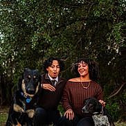 Koa joined the competition — help win amazing prizes! couple, man, woman, dogs, dog, outdoor, trees, grass, portrait, pets, leash, collar, sitting, kneeling, surprised_expression, smiling, curly_hair, sweater, necklace, blurred_foreground