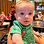 Mateo joined the competition — help win amazing prizes! adult_in_background, arm, baby, big_eyes, bokeh, child, closeup, crowd, cute, dining, green_onesie, hand, held, indoor, infant, looking_at_camera, portrait, restaurant, table, wood_paneling