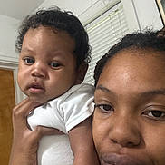 Kyndyl is registered to the contest to win money with this photo: baby, woman, indoor, close_up, portrait, holding, child, person, face, expression, window, door, white_clothing, braids, skin, hand, young, casual, family, together