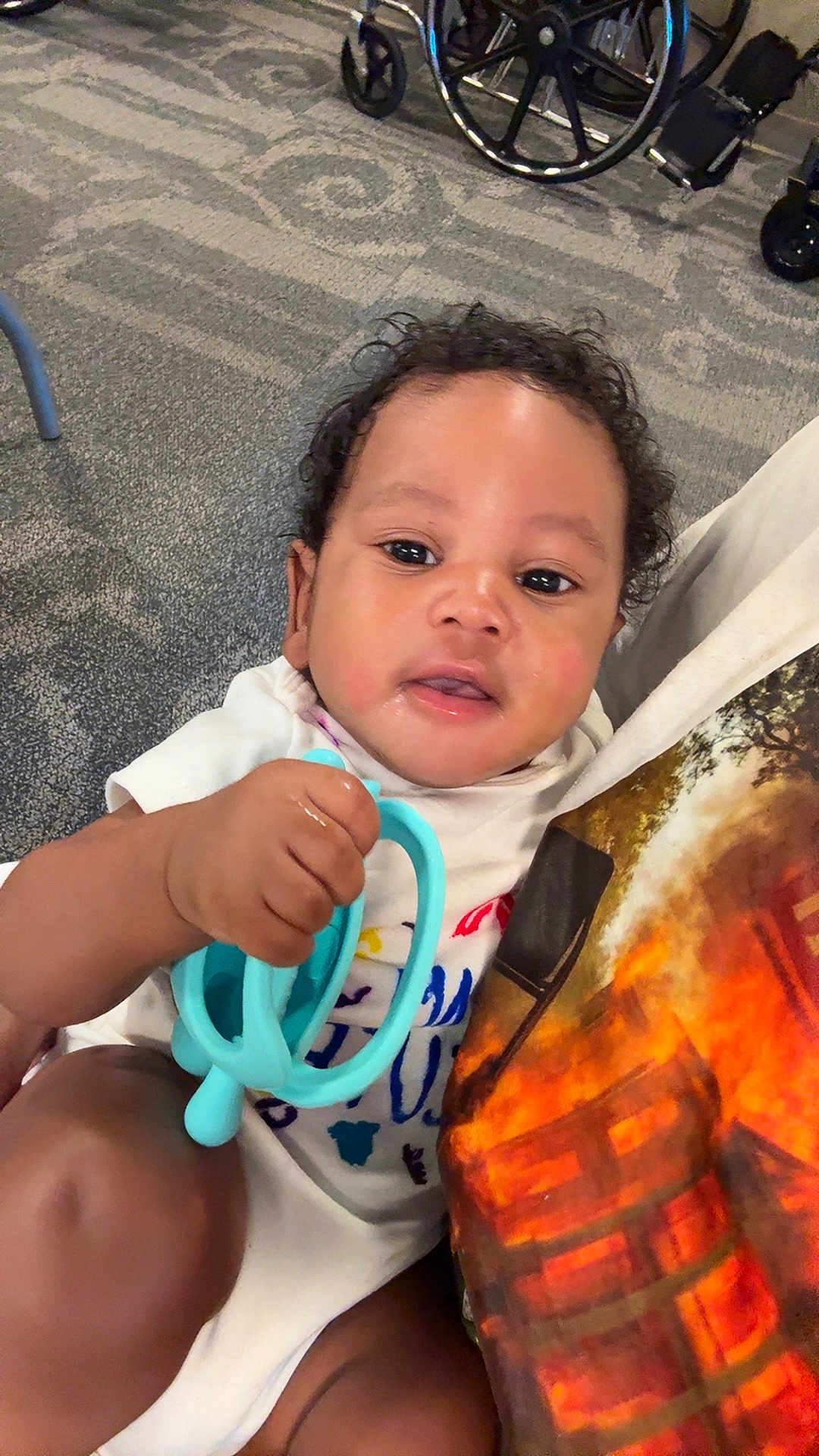 Kyndyl joined the competition — help win amazing prizes! baby, child, curly_hair, toy, blue, hand, face, person, clothing, sitting, lap, indoor, carpet, pattern, skin, cute, expression, holding, young, portrait