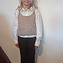 black_pants, blonde_hair, carpet, casual, child, clothing, feet, floor, girl, indoor, knitted_vest, person, plain_wall, portrait, shadow, smile, standing, white_shirt, white_shoes, young