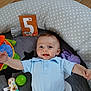baby, child, smiling, blue_shirt, play_mat, toys, polka_dot, cushion, floor, wooden_floor, green_ball, stuffed_animal, purple_toy, happy, lying_down, infant, portrait, indoor, cute, polo_shirt