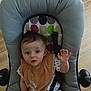 baby, infant, child, baby_seat, bib, polka_dot, wooden_floor, curious, face, hand, clothing, indoor, person, seat_belt, expression, young_child, cute, sitting, looking_up, raised_hand