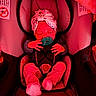 Naomi is registered to the contest to win money with this photo: baby, car_seat, pacifier, head_wrap, sleeping, infant, clothing, socks, baby_carrier, child, seat_belt, pink, red_light, indoors, soft_fabric, cozy, resting, newborn, cute, portrait