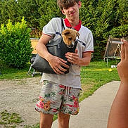 Heïko a rejoint le concours — aidez-le/la à gagner de superbes lots ! young_man, puppy, handbag, outdoor, garden, greenery, shorts, white_shirt, casual, summer, photography, phone, person, grass, trees, smile, funny_pose, daylight, barefoot, playing