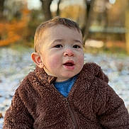 Kinay participe au concours pour gagner de l'argent avec cette photo : child, toddler, outdoor, autumn, snow, brown_jacket, fuzzy_clothing, cute, curious, face, portrait, nature, trees, blurred_background, winter_clothing, young_child, expression, sitting, seasonal, warm_clothes