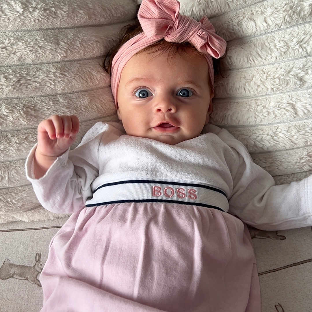 Amelia joined the competition — help win amazing prizes! adorable, baby, blanket, bunny_print, child, clothing, cute, dress, face, headband, indoors, infant, looking_at_camera, lying_down, person, pink_bow, portrait, small_hands, soft_texture, wide_eyes