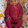 baby, child, infant, sitting, smiling, portrait, indoors, blanket, bed, onesie, pink_clothing, hair_bow, dark_skin, face, hands, feet, cozy, colorful, home, photography