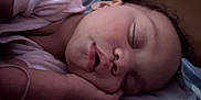 Brayah is registered to the contest to win money with this photo: baby, sleeping, face, hand, curly_hair, mouth, bed, bedding, pillow, resting, peaceful, child, indoors, closeup, soft_light, skin, person, young, quiet, comfort