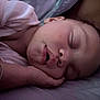 baby, sleeping, face, hand, curly_hair, mouth, bed, bedding, pillow, resting, peaceful, child, indoors, closeup, soft_light, skin, person, young, quiet, comfort