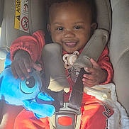 Demari joined the competition — help win amazing prizes! baby, blanket, blue_toy, car_seat, child, cute, face, hand, happy, indoors, infant, pacifier, person, red_clothing, safety_harness, seat, seat_belt, smile, stuffed_toy, sunlight