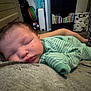 baby, sleeping, infant, pajamas, striped_clothing, person, hand, indoor, bedroom, furniture, bookshelf, book, home, rest, peaceful, child, portrait, human, skin, comfort